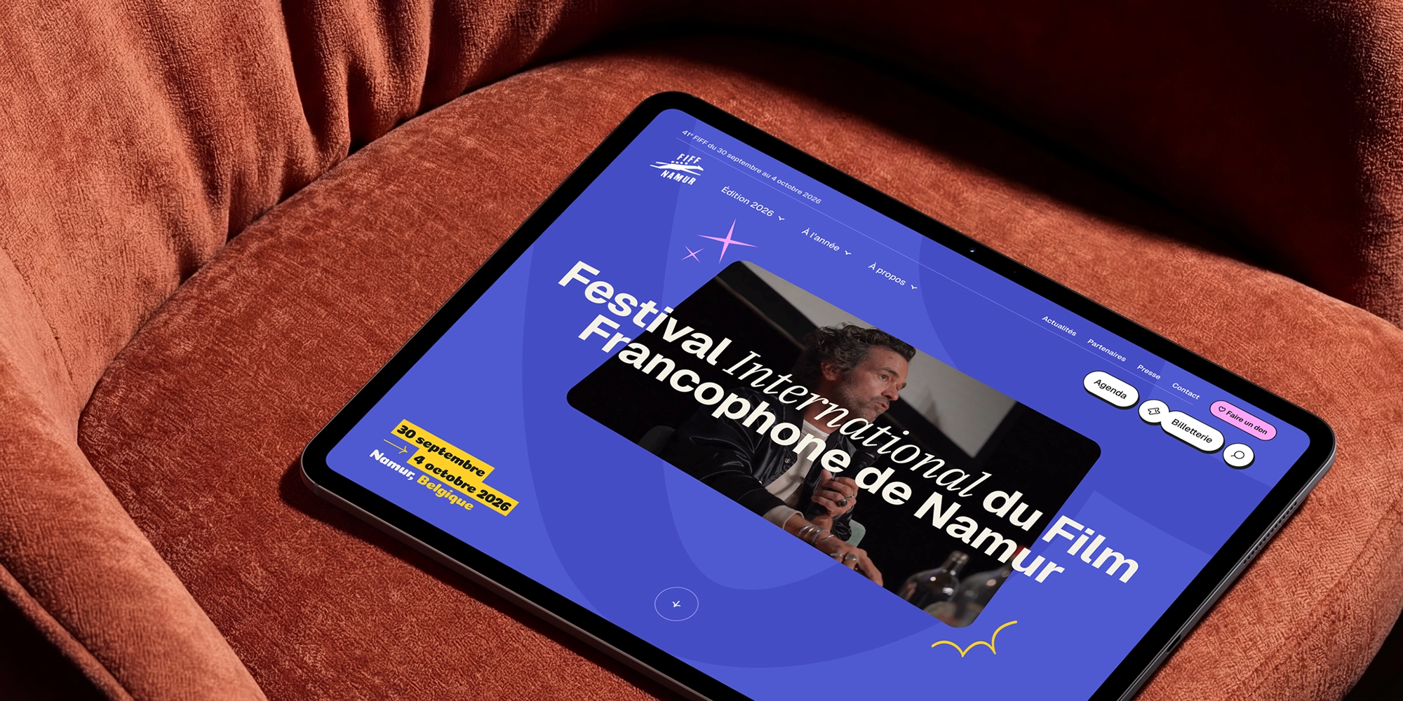Tablette posée sur un fauteuil rouge affichant la page d’accueil du Festival International du Film Francophone de Namur 2026.